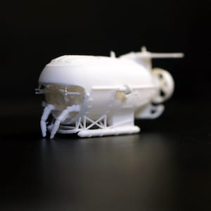 Peut inclure: Maquette blanche de sous-marin, avec une coque arrondie, des hélices et des bras articulés. Le modèle est présenté sur un fond sombre, mettant en valeur son design et ses détails.