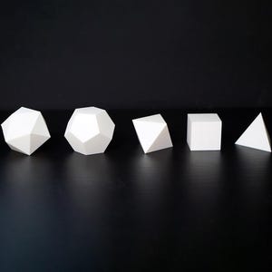 Puede incluir: Seis formas geométricas blancas, incluyendo un dodecaedro, un cubo y una pirámide, están dispuestas sobre una superficie negra. Las formas están espaciadas uniformemente y parecen estar hechas de un material sólido. La iluminación resalta los bordes y facetas de cada forma.