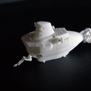 Peut inclure: Maquette de sous-marin blanc avec des détails tels qu'une tour de contrôle, des structures rectangulaires et une hélice. Le sous-marin miniature a un petit bras qui s'étend sur le côté. Le modèle est posé sur un fond sombre.