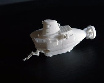 Könnte beinhalten: Ein weißes Modell-U-Boot mit detaillierten Merkmalen, darunter ein Turm, rechteckige Strukturen und ein Propeller. Das Miniatur-U-Boot hat einen kleinen Arm, der sich von der Seite erstreckt. Das Modell ist vor einem dunklen Hintergrund platziert.