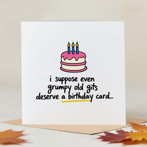 Può includere: Biglietto di compleanno bianco con un'illustrazione di torta e la scritta "i suppose even grumpy old gits deserve a birthday card..." La torta ha glassa rosa e tre candele blu.