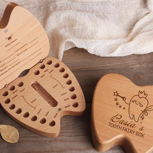 May include: Wooden tooth fairy box with a tooth-shaped design. The box is open, revealing a compartment for baby teeth. The lid has space for baby's information. The closed box has a tooth fairy illustration and the text "Basia's Tooth Fairy Box."