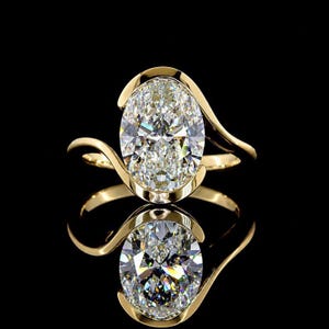 Könnte beinhalten: Ein Goldring mit einem großen, oval geschliffenen, klaren Edelstein in einer Ringschiene im Bypass-Stil. Die polierte Goldschiene schwingt sich um die Ober- und Unterseite des zentralen Steins und bildet einen eleganten Rahmen auf Schwarz.