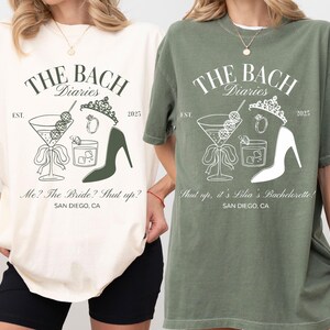 May include: Two oversized t-shirts, one ivory and one moss green, featuring a graphic design for a bachelorette party. The design includes a martini glass, high heel, and text that reads "The Bach Diaries" and "San Diego, CA."