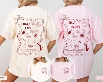 May include: Ivory and pink t-shirts with a graphic design for a bachelorette party. The ivory shirt says "Lucky in Love" and the pink shirt says "Just Lucky." Both shirts have a Las Vegas theme.