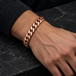 May include: A polished rose gold-tone curb chain bracelet featuring interlocking, rounded metal links. The bracelet has a high-shine, reflective finish and is secured around the wrist. The text TheGemsHubArt is visible in the upper right corner.