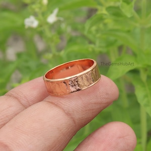 May include: A copper-coloured ring with a hammered, textured exterior surface and a smooth, polished interior band. The metal has a warm, metallic reddish-brown tone. The text TheGemsHubArt is visible in the upper right corner of the image.