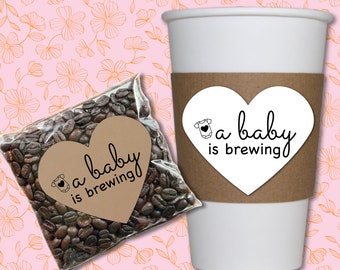 May include: A brown paper bag filled with coffee beans with a heart-shaped sticker that says "a baby is brewing" and a white coffee cup with a brown sleeve with a heart-shaped sticker that says "a baby is brewing".