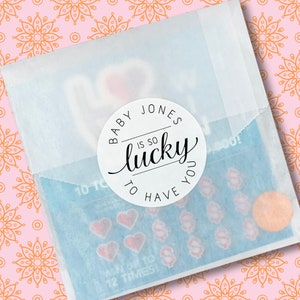 May include: A white sticker with black text that reads "Baby Jones is so lucky to have you". The sticker is on a blue and white background with hearts and dollar signs.