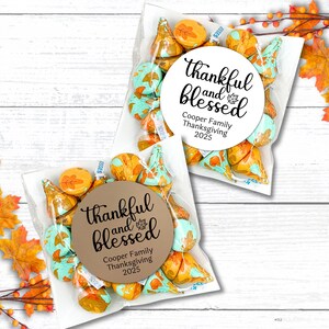 May include: Two clear cellophane bags filled with Hershey's Kisses candies. The candies are a mix of orange, teal, and gold foil wrappers. Each bag has a round sticker that reads "thankful and blessed" with "Cooper Family Thanksgiving 2025".