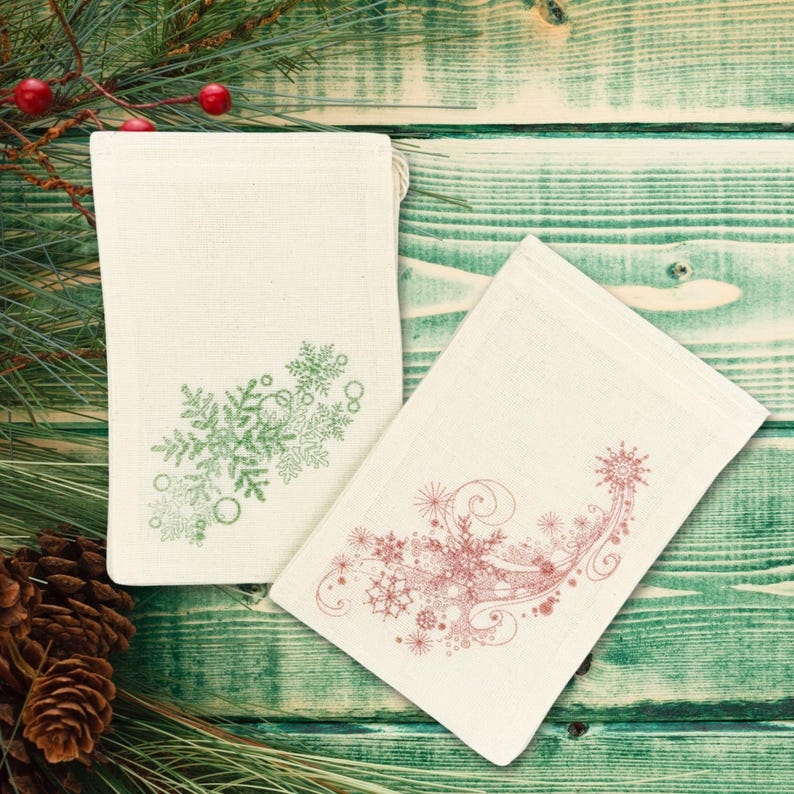 K&ouml;nnte beinhalten: Zwei wei&szlig;e Stoffgeschenkt&uuml;ten mit Kordelzug. Eine Tasche hat ein gr&uuml;nes Schneeflockenmuster und die andere ein rotes Schneeflockenmuster.