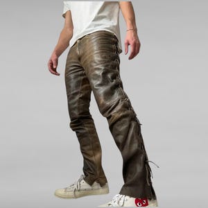 May include: Brown leather pants with lace-up detailing on the sides. The pants have a distressed, vintage look and are paired with white sneakers. The leather pants are a unique fashion statement.