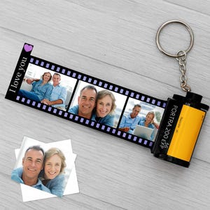 May include: A personalised film strip keyring with three photo slots and a film canister charm. The film strip has the words "I love you" and a purple heart. A unique gift idea.