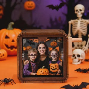 May include: A wooden Halloween photo frame featuring a family portrait. The square frame has a dark brown finish. The photo shows a woman and two children in Halloween costumes, with pumpkins and bats in the background. A black spider is in the foreground.