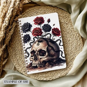 May include: A spiral-bound notebook with a skull design, from which red and black roses emerge. The notebook has a white background and the words "EXAMPLE OF USE" at the bottom. The roses provide a striking contrast against the skull.