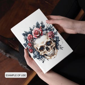 May include: A white journal featuring a skull design adorned with red roses and dark blue leaves. The words "EXAMPLE OF USE" are printed on the bottom. The journal is held in a person's hands.