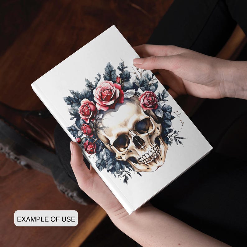 May include: A white journal featuring a skull design adorned with red roses and dark blue leaves. The words "EXAMPLE OF USE" are printed on the bottom. The journal is held in a person's hands.