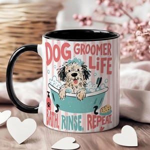Könnte beinhalten: Ein weißer Keramikbecher mit schwarzem Henkel und schwarzem Innenraum, verziert mit einer Grafik eines zotteligen Hundes in einer türkisfarbenen Badewanne voller Schaum. Der Text lautet "DOG GROOMER LIFE" und "BATH. RINSE. REPEAT." auf rosa Streifen.
