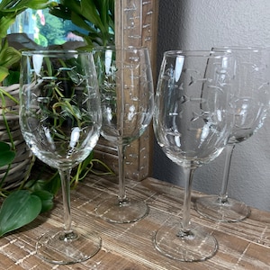 May include: A set of four clear glass wine glasses, each featuring a delicate etched pattern of small fish swimming in various directions. The glasses have a classic rounded bowl shape, a slender stem, and a stable circular base, providing a consistent look.
