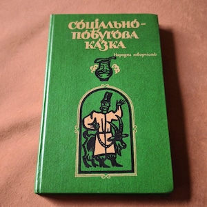 May include: A green book with the title "СОЦІАЛЬНО-ПОБУТОВА КАЗКА" in white letters. The cover features an illustration of a man with a goat inside a black and gold frame. The words "Народна творчість" are also present.