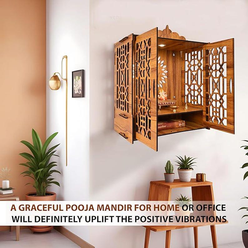 Puede incluir: Un Pooja Mandir de pared de madera con intrincados cortes geom&eacute;tricos en las puertas. Las puertas abiertas revelan un peque&ntilde;o estante con objetos religiosos. El Mandir est&aacute; hecho de madera marr&oacute;n claro y est&aacute; montado en una pared blanca. El texto en la parte inferior dice: A GRACEFUL POOJA MANDIR FOR HOME OR OFFICE WILL DEFINITELY UPLIFT THE POSITIVE VIBRATIONS.