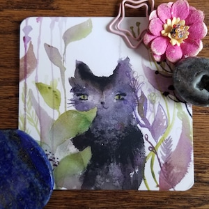 May include: A watercolor painting of a black cat with green eyes, surrounded by purple and green foliage. The cat is looking directly at the viewer.