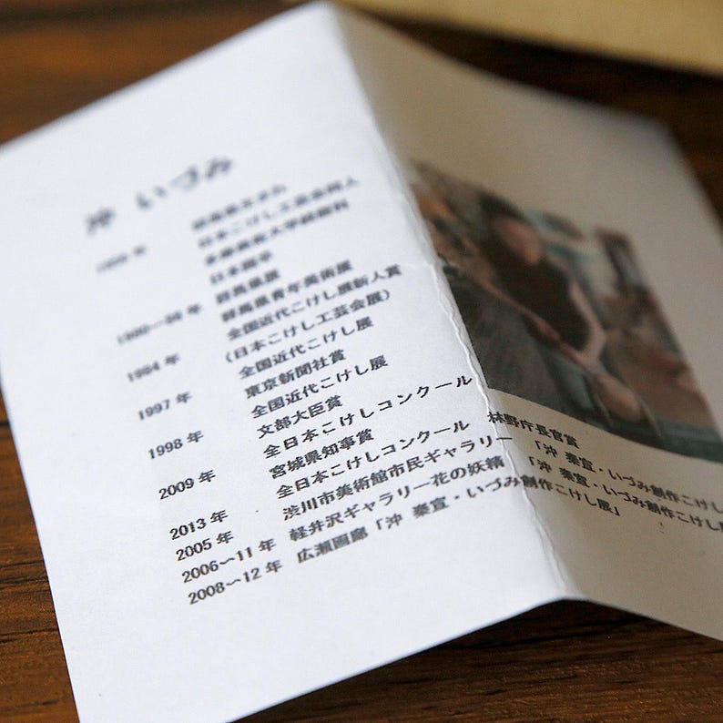 May include: A white brochure with Japanese text and a photograph. The brochure is open, revealing text on the left side and a blurred image on the right. The text includes dates and awards.