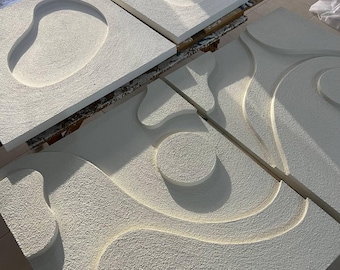 Op de afbeelding: Vier witte, getextureerde wandkunstwerken met abstracte, verhoogde ontwerpen. De stukken hebben organische vormen, waaronder cirkels en vloeiende lijnen, die een gevoel van diepte en dimensie creëren. De kunst wordt gepresenteerd op een lichtgekleurd oppervlak.