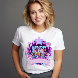 Puede incluir: Camiseta blanca con un diseño gráfico colorido que dice "KPOP DESIGN". El diseño incluye una estrella, notas musicales, bolas de discoteca y una pancarta. El gráfico muestra tres figuras en una ilustración estilizada.