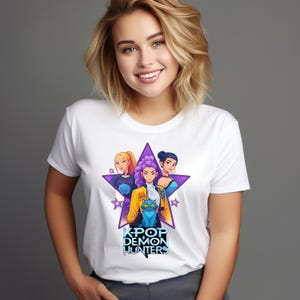 Puede incluir: Camiseta blanca con un diseño de estrella púrpura que presenta a tres mujeres de estilo anime y un gato azul. El texto "KPOP DEMON HUNTERS" está debajo. Cuello redondo.