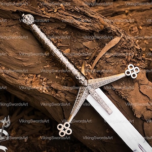May include: A silver sword with an elaborate handle and crossguard, displayed on a weathered wooden surface. The blade is bright, and the design includes intricate patterns. The sword is a symbol of strength.