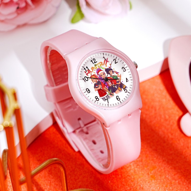 May include: A light pink wristwatch with a white watch face featuring a colorful illustration of people. The watch has a matching pink band and a classic analog display with black numerals and hands.