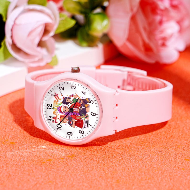 May include: A light pink wristwatch with a white watch face featuring a colorful cartoon design. The watch has a matching pink band and a silver-colored crown. The watch face displays the numbers 1 through 12.
