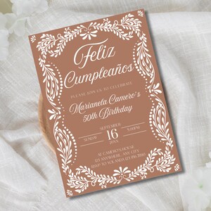 Peut inclure: Une invitation d'anniversaire de couleur terre cuite avec une bordure florale blanche et du texte. L'invitation indique "Feliz Cumplea&ntilde;os" et annonce le 50e anniversaire de Marianela Camero, avec la date, l'heure et le lieu.