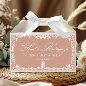 Puede incluir: Una caja blanca con asa de cinta de satén, con una etiqueta rosa empolvado con bordes blancos ornamentados, una cruz, una paloma, el texto: Amelia Rodriguez's BAPTISM & FIRST BIRTHDAY, APRIL 24TH, 20XX, y la imagen de la Virgen de Guadalupe.