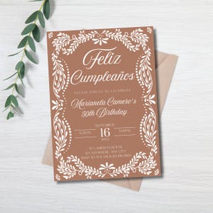 Peut inclure: Une invitation d'anniversaire de couleur terre cuite avec une bordure florale blanche et du texte. L'invitation indique "Feliz Cumplea&ntilde;os" et invite les invit&eacute;s &agrave; c&eacute;l&eacute;brer le 50e anniversaire de Marianela Camero le 16 septembre &agrave; 17h00. L'invitation est sur une enveloppe neutre.