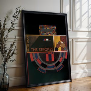 May include: Framed art print of "Room on Fire" by The Strokes. The artwork features a black background with geometric shapes in red, blue, and yellow. The band's name is displayed in a stylized font. The print is in a black frame.