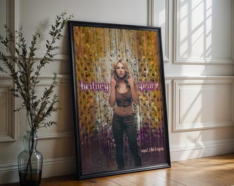 May include: Framed poster featuring Britney Spears. The image shows Spears in a brown top and trousers, with the words "britney spears" in purple. The background has a gold and silver beaded curtain effect. The text "oops!...I did it again" is at the bottom.