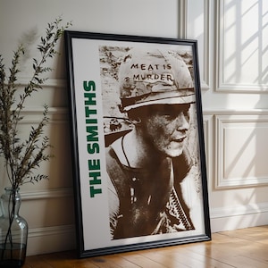 Puede incluir: Póster enmarcado con una imagen en tonos sepia de una persona con un casco militar con las palabras "MEAT IS MURDER". El nombre de la banda "THE SMITHS" está impreso verticalmente en verde. El póster está en un marco negro.