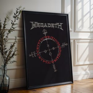 Puede incluir: Un póster negro enmarcado con el nombre de la banda "Megadeth" en letras plateadas. Debajo, un diseño circular con las palabras "Cryptic Writings" en rojo rodea un gráfico tipo brújula. El póster está apoyado contra una pared blanca.