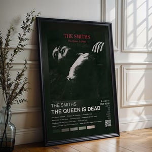 Peut inclure: Une affiche encadrée pour l'album "The Queen Is Dead" des Smiths. L'affiche présente une image en noir et blanc d'une personne et le titre de l'album en texte blanc et rouge. L'affiche est exposée sur un sol en bois à côté d'un vase avec des branches.