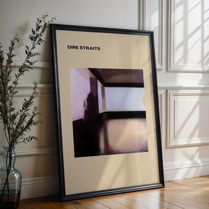 May include: Framed art print featuring the text "DIRE STRAITS" at the top. The artwork depicts an abstract interior scene with muted tones of beige, brown, and white. The print is displayed in a black frame, leaning against a wall.