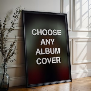 May include: A framed poster with the words "CHOOSE ANY ALBUM COVER" in white block letters against a dark, gradient background. The frame is black, and the poster is leaning against a white wall and wooden floor.