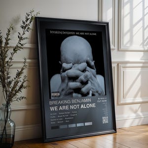 May include: Framed poster for the album "We Are Not Alone" by Breaking Benjamin. The black and white image features a person with their hands covering their face. The poster includes the album title, song titles, and a QR code.