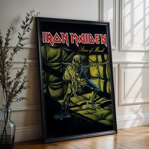 May include: Black framed poster with the Iron Maiden logo in red and the album title "Piece of Mind." The image shows a zombie-like figure in chains on a green, tufted background. A classic rock music poster.