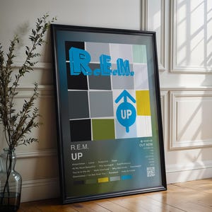 May include: Framed poster featuring the band R.E.M.'s album "Up." The poster has a black frame and a colorful design with the band's name in blue 3D lettering. The album title "UP" is in a blue circle with an upward arrow.