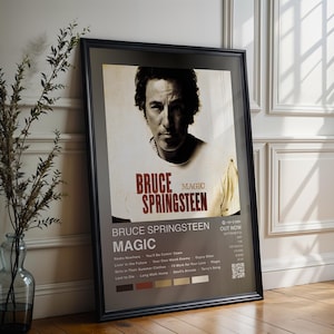 Op de afbeelding: Een ingelijste poster met Bruce Springsteen en de albumtitel "Magic". De poster toont een sepia-afbeelding van Springsteen en een lijst met songtitels. De zwarte lijst staat tegen een witte muur.