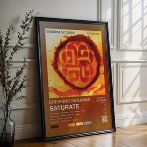 May include: Framed poster for the band Breaking Benjamin's album "Saturate." The poster features a burnt orange and yellow design with the band's name and album title in white text. Additional text includes song titles and release information.