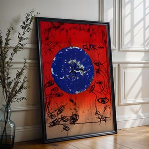 May include: Framed art print with a vibrant red and orange background, featuring a large blue circle with a starburst design. Black line art of eyes and abstract shapes surrounds the circle. The text "CURE wish" is visible.
