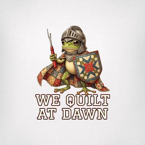 May include: A green frog wearing a metal knight helmet and a colorful patchwork quilt cape, holding a red-handled seam ripper and a matching patchwork shield, with the text WE QUILT AT DAWN printed in bold letters below the figure.